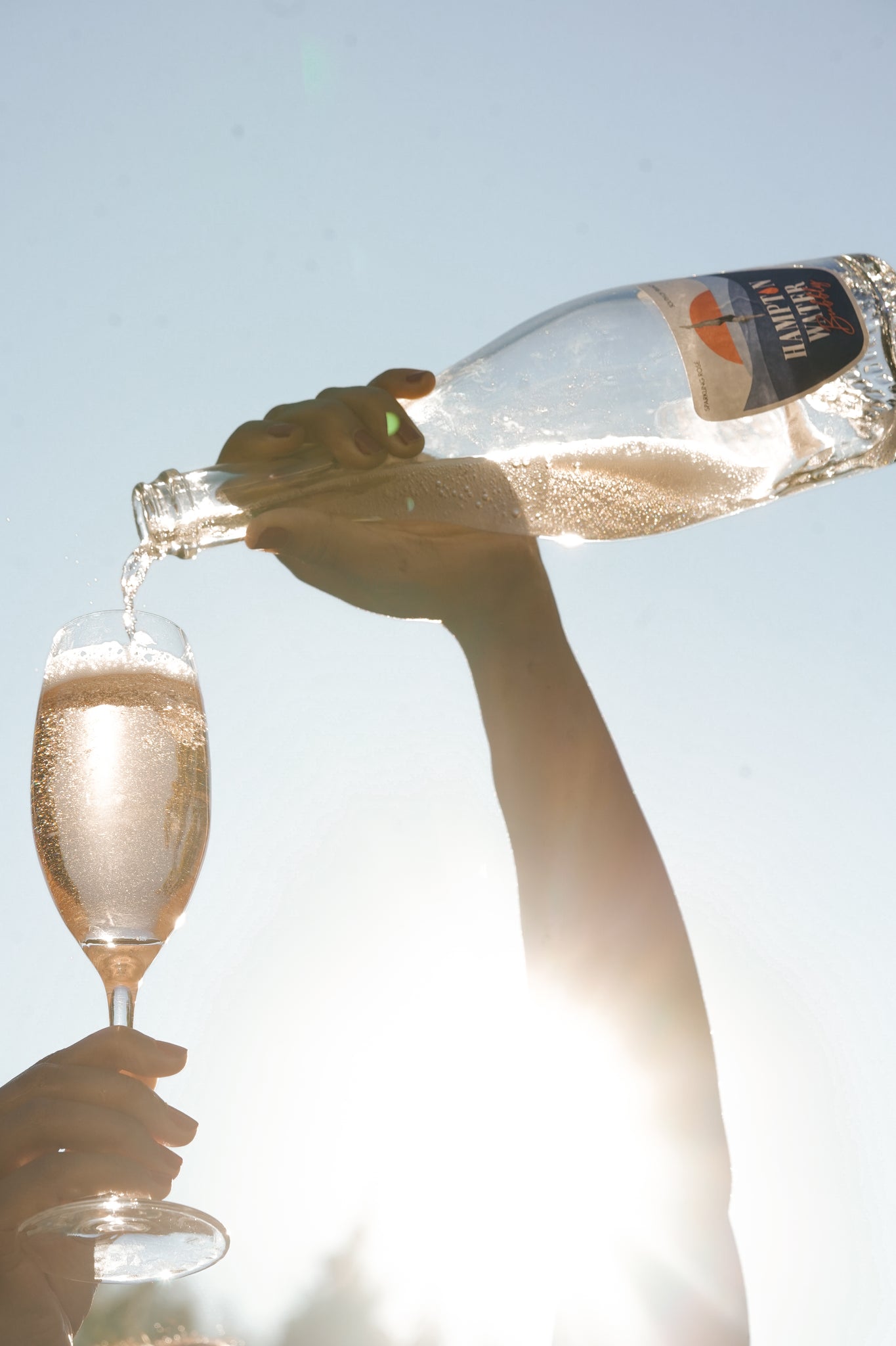 Arm holding a bottle and pouring a large glass of Hampton Water Bubbly