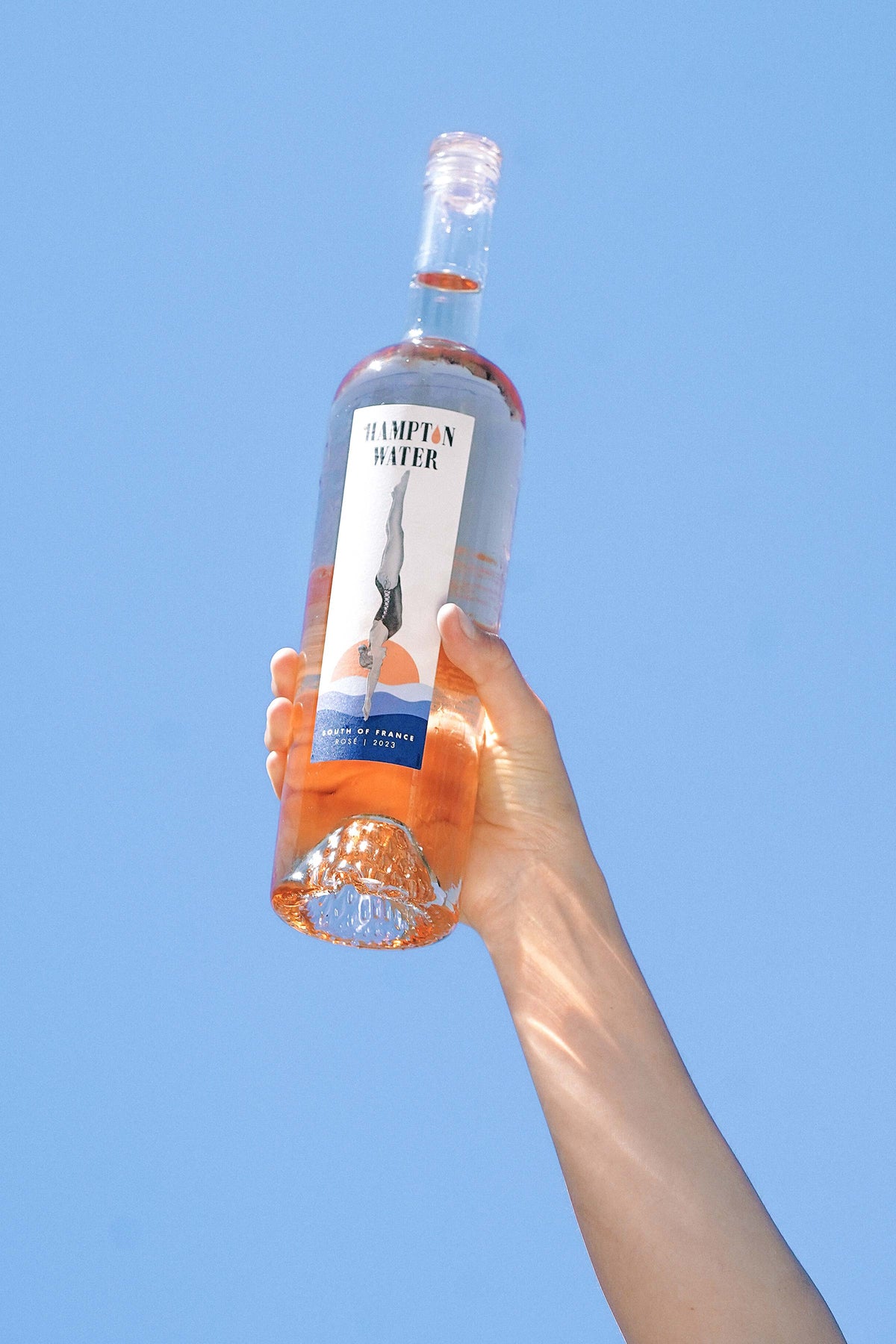 Arm holding up a bottle of Hampton Water Rosé to the sky